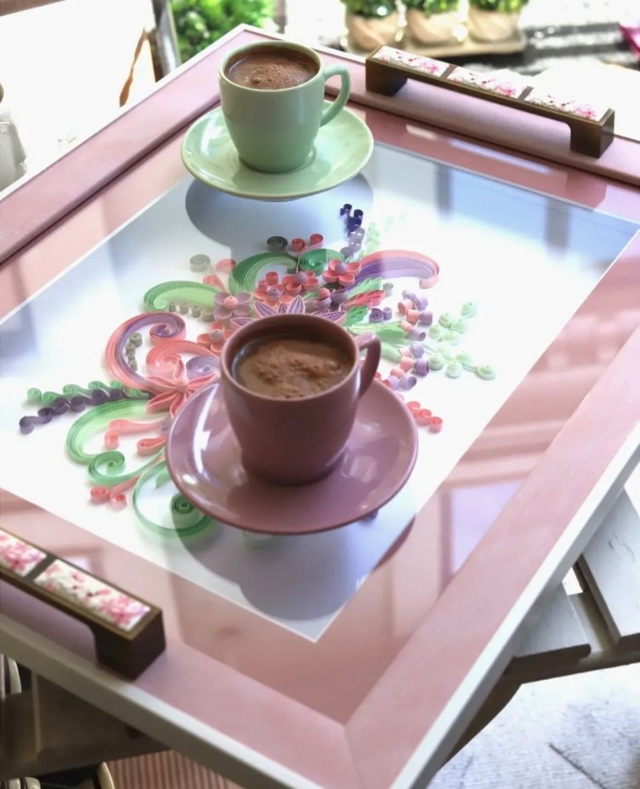 Pembe çerçeveli quilling tepsi üzerinde iki fincan kahve; camın altında lila, pembe ve yeşil kâğıt çiçekler